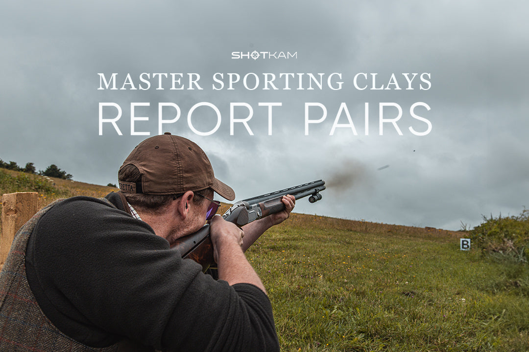 Man in cap and shooting vest practicing transitions between report pairs on grassy shooting course