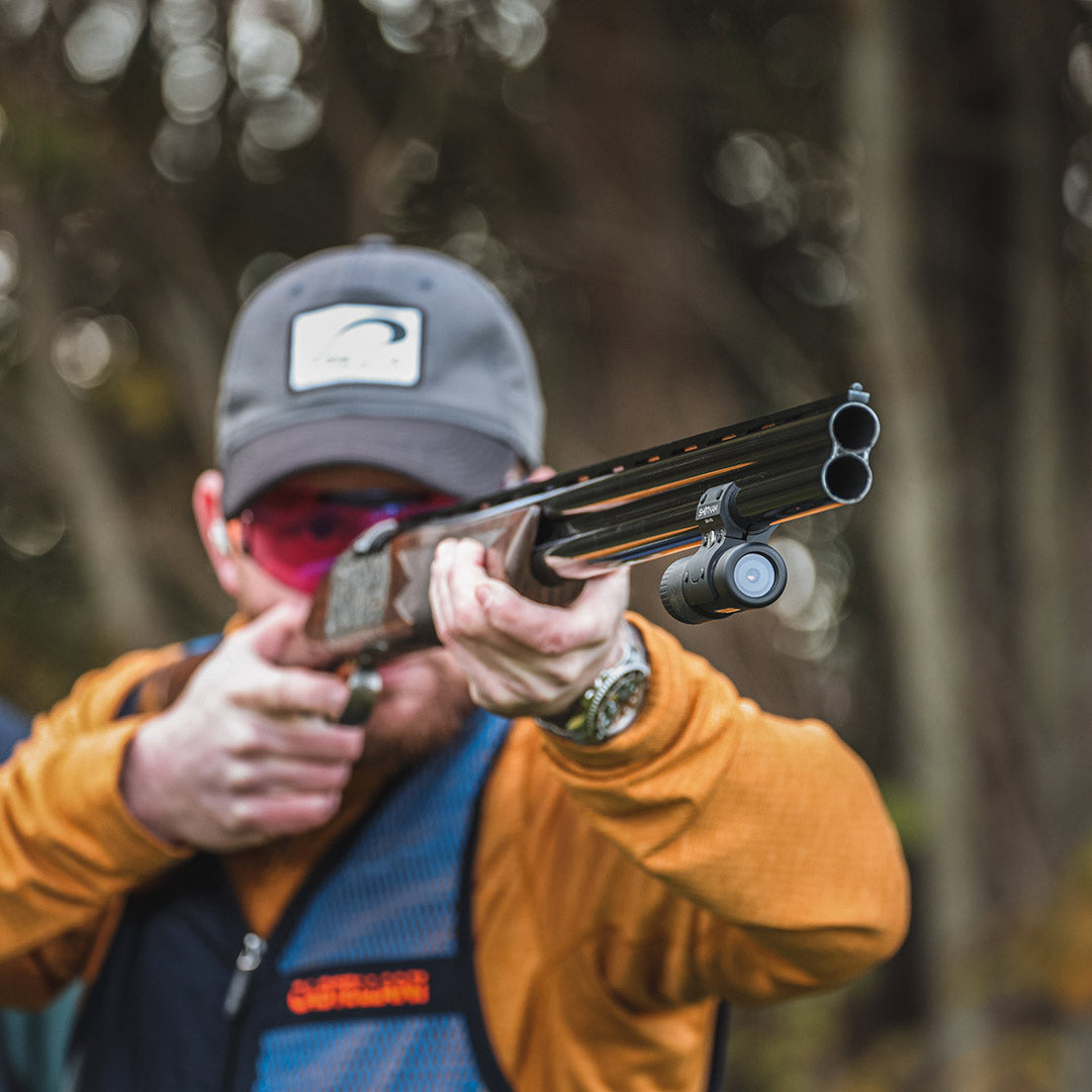 Shooter in CA using a ShotKam Gen 4 Mini on an over-and-under shotgun, aiming at a target during a sporting clays event, wearing pink-tinted glasses.