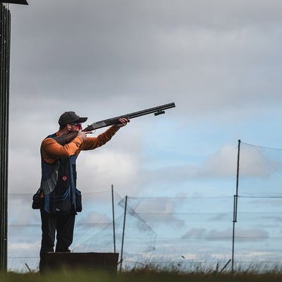 Clay shooter in CA uses a ShotKam Gen 4 Mini on an over-and-under shotgun during a sporting clays event, standing on a platform under a cloudy sky.