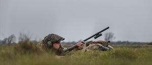 Person in camouflage gear with a rifle in a grassy field with ShotKam
